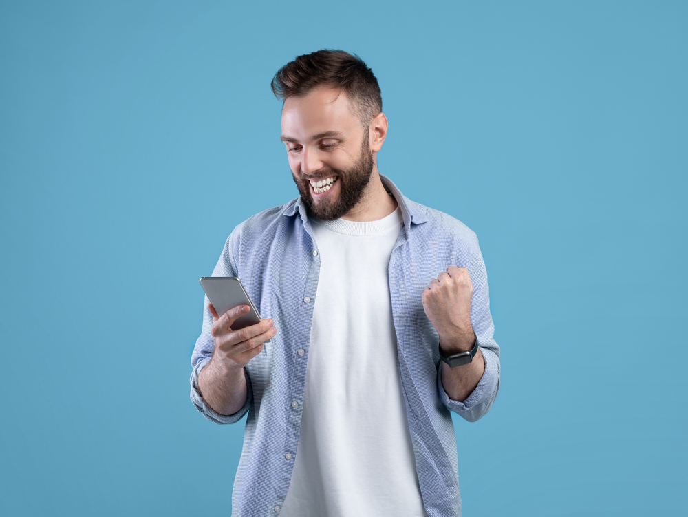 Portrait,Of,Happy,Bearded,Young,Man,Using,Smartphone,,Making,Winner
